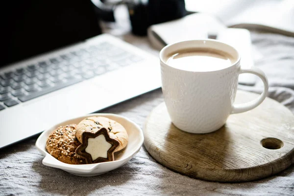 Echter Arbeitsplatz zu Hause, Laptop mit Tasse Kaffee und Keksen auf dem Bett mit kuscheliger Decke — Stockfoto