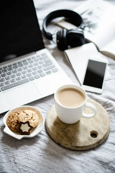 Real home workplace, laptop with cup of coffee with cookies on bed with cozy blanket