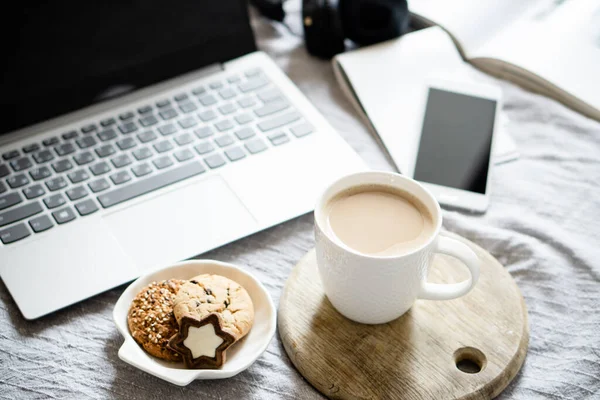 Real home workplace, laptop with cup of coffee with cookies on bed with cozy blanket