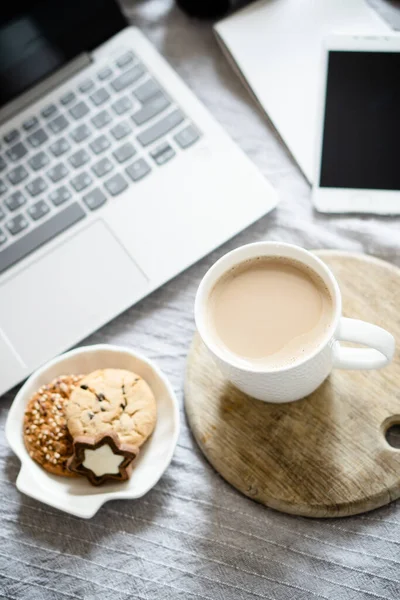 Real home workplace, laptop with cup of coffee with cookies on bed with cozy blanket — Stock Photo, Image