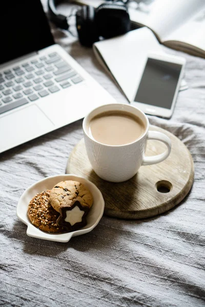 Real home workplace, laptop with cup of coffee with cookies on bed with cozy blanket