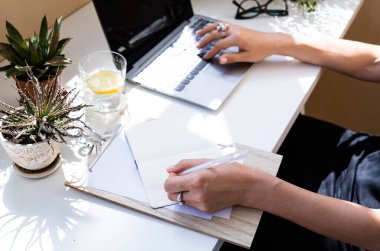 Kadınlar ellerini dizüstü bilgisayara koyup not defterine yazıyorlar.