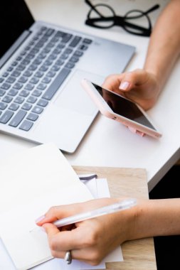 Kadınların el ele tutuşması akıllı telefon ve not defterine not düşmesi rahat yaz ofisinde dizüstü bilgisayarla