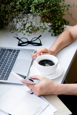 Kadınlar rahat ofiste ellerinde kahve ve akıllı telefonlar, dizüstü bilgisayarlar ve yeşil bitkilerle.