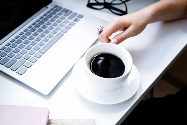 Frauenhände mit Kaffeetasse im gemütlichen Büro mit Laptop und grünen Pflanzen — Stockfoto