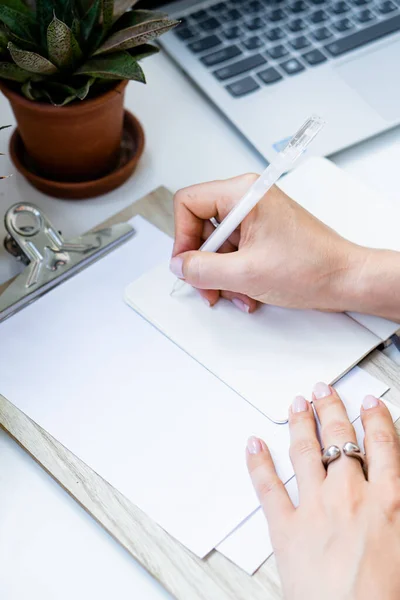 Kadın elleri, rahat yaz ofisinde dizüstü bilgisayar ve yeşil ev bitkileriyle not defterine not alıyor. — Stok fotoğraf
