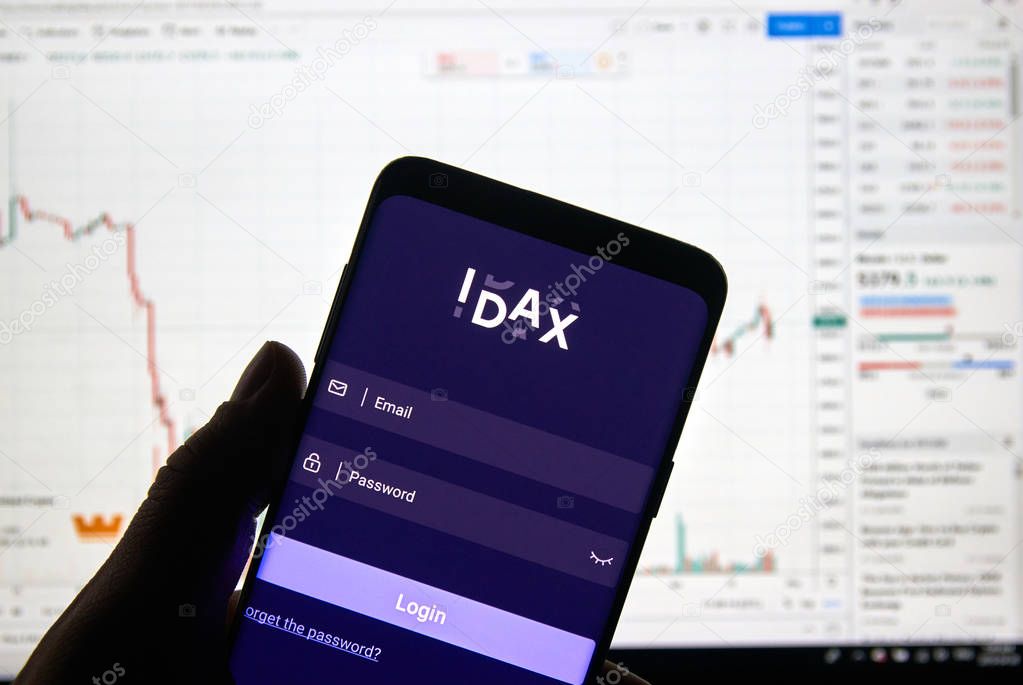 MONTREAL, CANADA - APRIL 26, 2019: IDAX cryptocurrency exchange logo and application on Android Samsung Galaxy s9 Plus screen in a hand over a laptop display with bitcoin chart on it.