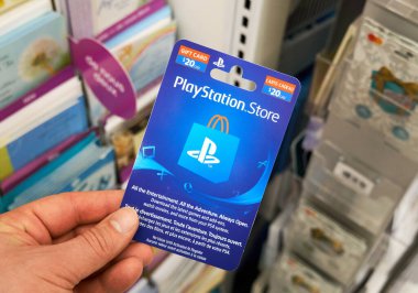Montreal, Canada - May 03, 2020: Playstation gift card in a hand over a stand with gift cards. Playstation is a popular video game console developed by Sony