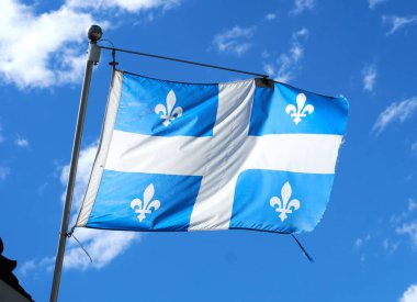 Mavi gökyüzü arkaplanı üzerinde sallanan Quebec bayrağı. Quebec bayrağı, Quebec Kanada 'nın Quebec eyaletini temsil eder, bayrak mavi arka planda beyaz bir haçtan oluşur.