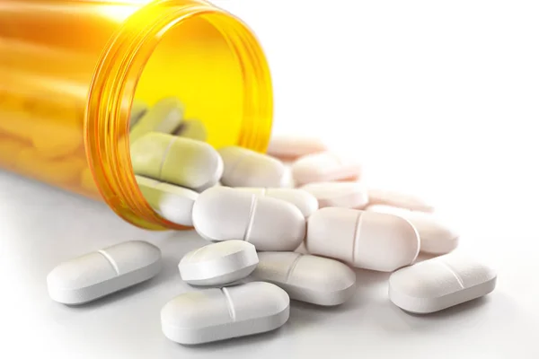 Pillen, die aus der Tablettenflasche auslaufen, isoliert auf weiß. Medizin und — Stockfoto