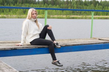 Üzgün genç kadın pier gölün üzerine oturuyor 