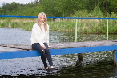 Üzgün genç kadın pier gölün üzerine oturuyor 