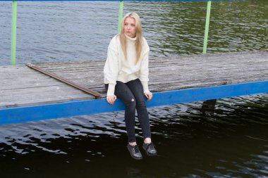 Üzgün genç kadın pier gölün üzerine oturuyor 