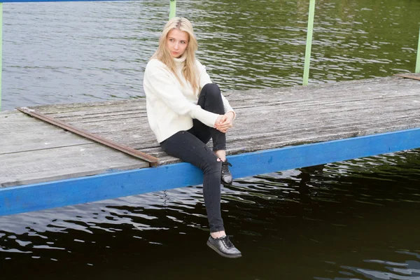 Üzgün genç kadın pier gölün üzerine oturuyor 