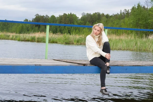 Üzgün genç kadın pier gölün üzerine oturuyor 