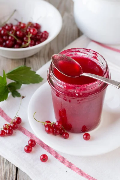 Red currant jam in glass jar on wooden table