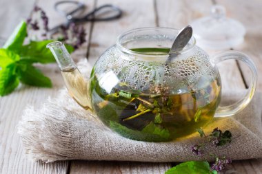 Naneli çay ve ahşap masadaki cam demlikte keklik otu.