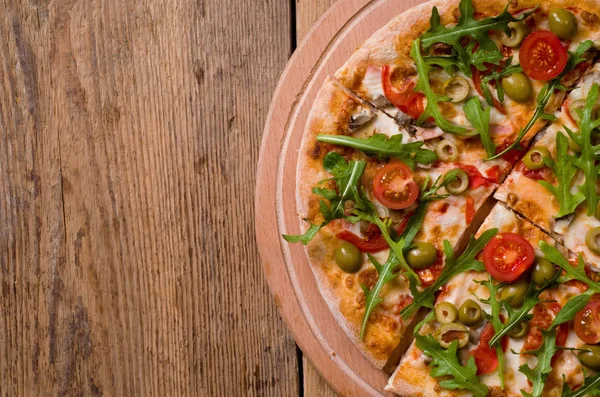 Roka ve domates pizza ahşap tahta üzerinde dilimlenmiş