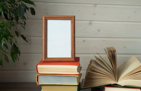 Photo frame and pile of old books on wooden table — Stock Photo, Image