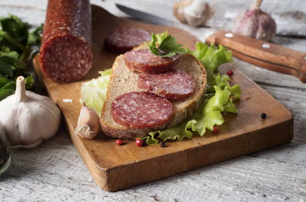 Salami y pan en una tabla de madera — Foto de Stock