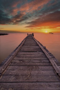 Old wooden pier stretching out into the sea with a dramatic sunset. clipart
