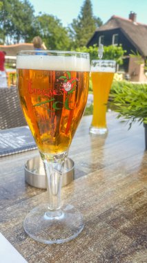 Giethoorn, Hollanda - 23 Ağustos 2017: Brugse Zot adlı taze Belçika birası bir bardakta servis edildi. Belçika 'nın Bruges şehrinde üretilen tek bira..