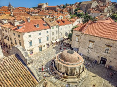 Dubrovnik, Hırvatistan - 24 Temmuz 2025: Büyük Onofrios Çeşmesi 'nin yanından geçen insanlar. Sekizgen havuz olarak yapılandırılmıştır, erkek çocukların, sütunların, yunusların ve deniz kabuklarının kabuklarıyla süslenmiştir..