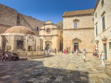 Dubrovnik, Hırvatistan - 24 Temmuz 2025: Büyük Onofrios Çeşmesi 'nin yanından geçen insanlar. Sekizgen havuz olarak yapılandırılmıştır, erkek çocukların, sütunların, yunusların ve deniz kabuklarının kabuklarıyla süslenmiştir..