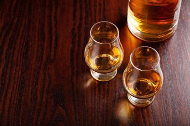 Koyu kahverengi arka planda bir şişe viski ve bir bardak brendi.