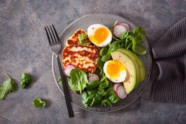 Sağlıklı keto paleo diyeti kahvaltısı: haşlanmış yumurta, avokado, halloumi peyniri, salata yaprakları.