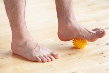 Adam evde masaj topu kullanarak düztaban düzeltme jimnastik egzersizi yapıyor.