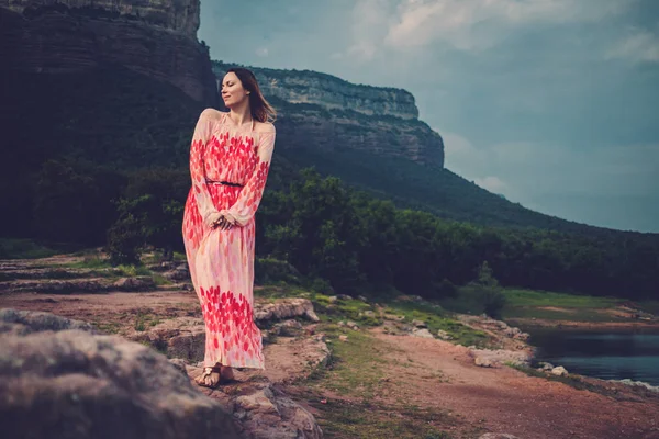 Jonge en mooie vrouw in rode jurk op zoek op bergen. Spanje, Sant Roma de Sau. — Stockfoto