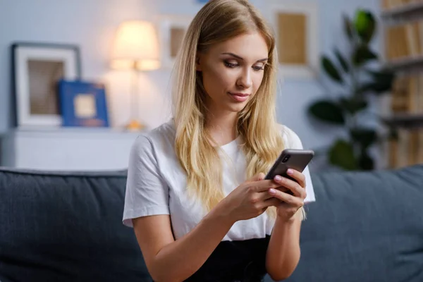 Vacker kvinna med hennes smartphone i vardagsrummet — Stockfoto