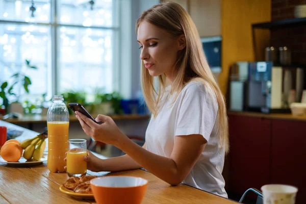 Mujer come el desayuno y utiliza su teléfono móvil —  Fotos de Stock