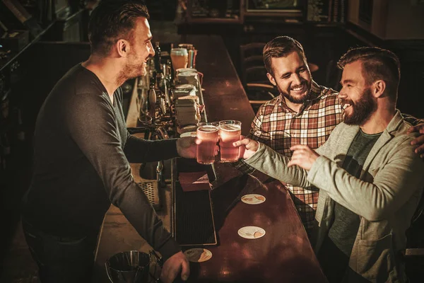 Старые друзья веселятся и пьют пиво за стойкой бара в пабе . — стоковое фото