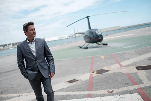 Бизнесмен разговаривает по мобильному телефону возле частного вертолета — стоковое фото