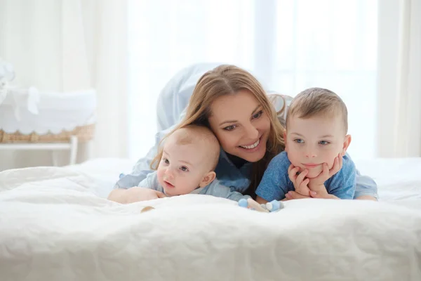 God middelaldrende mor med sine barn i en seng – stockfoto