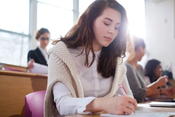 Belle fille prenant des notes dans un groupe multinational d'étudiants dans un auditorium — Photo