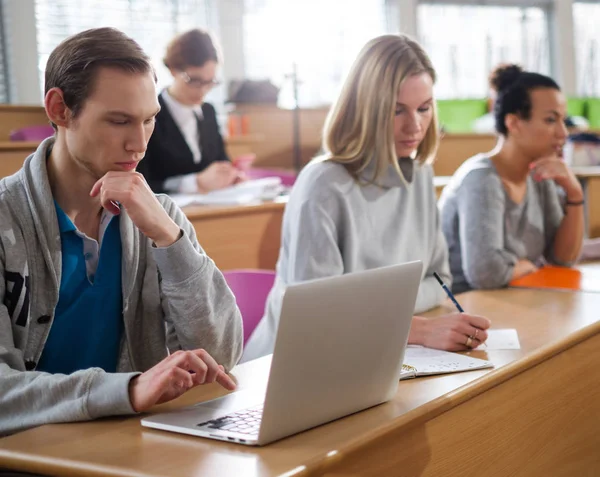Homem com laptop entre estudantes em um auditório — Fotografia de Stock
