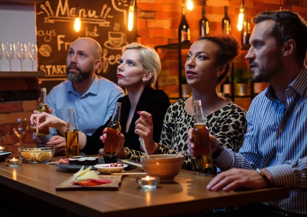 Группа друзей смотрит телевизор в кафе за барной стойкой — стоковое фото