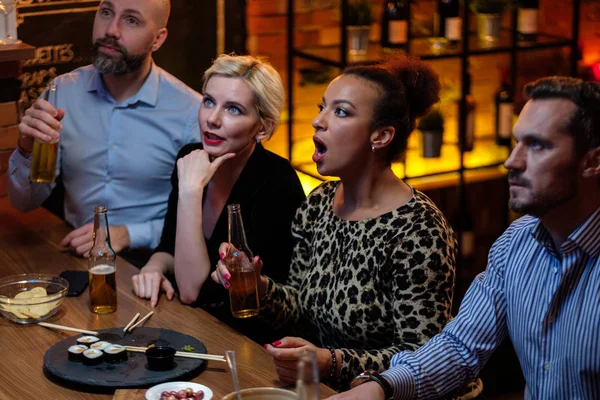 Группа друзей смотрит телевизор в кафе за барной стойкой — стоковое фото