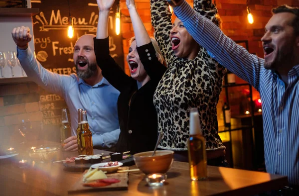 Grupo de amigos viendo la televisión en un café detrás del mostrador de bar —  Fotos de Stock