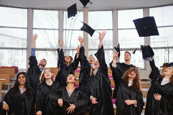 Multi grupo étnico de estudiantes graduados lanzando sombreros —  Fotos de Stock