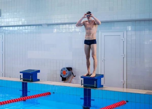 Nadador muscular se preparando para saltar do bloco inicial em uma piscina — Fotografia de Stock