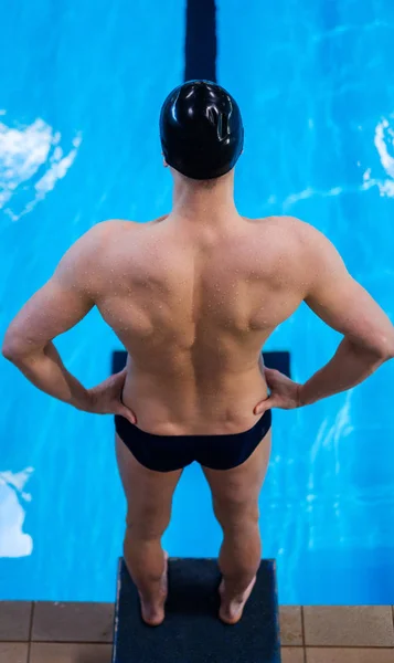 Мышечный пловец готовится к прыжку из стартового блока в бассейн — стоковое фото