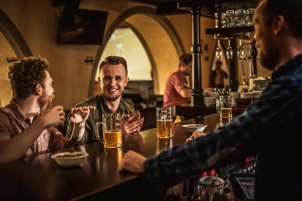 Amigos alegres bebendo cerveja rascunho em um bar — Fotografia de Stock