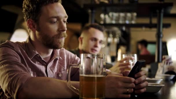 Un homme avec un téléphone portable buvant de la bière dans un pub — Video