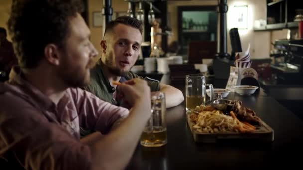 Веселые друзья пьют пиво и едят закуски в пабе — стоковое видео