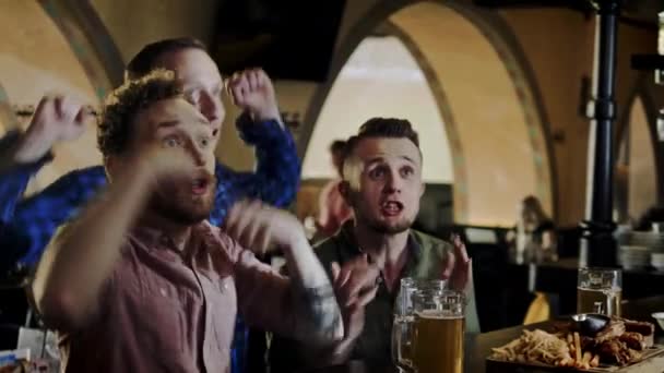 Vrienden drinken bier van de tap en tv kijken in een pub — Stockvideo