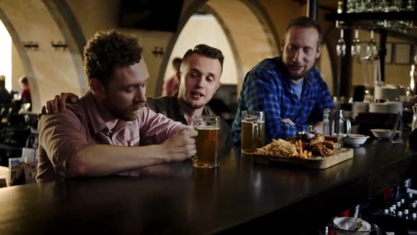 Amigos alegres bebiendo cerveza de barril y comiendo bocadillos en un pub — Vídeo de stock